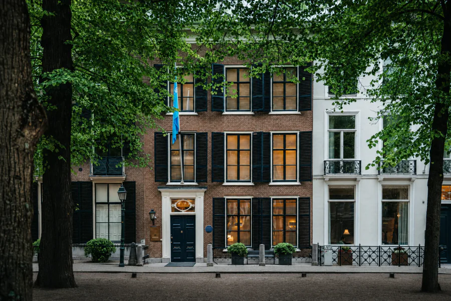 De monumentale gevel van Lange Voorhout 18 met blauwe vlag, onder groene lindes